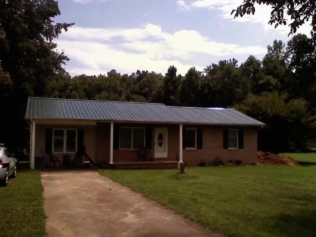 Dark green metal roof on a brick ranch with a covered porch in Grafton
