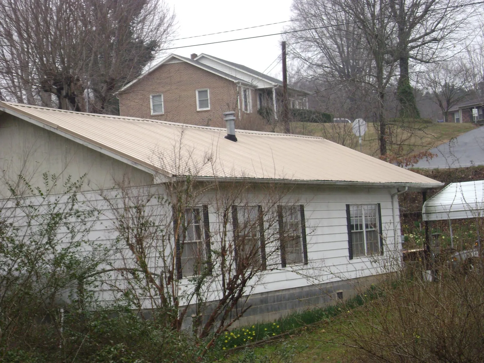 Tan metal roof on a white sided house set into a hillside — Commercial Roofing by Roofing Brothers in Grafton